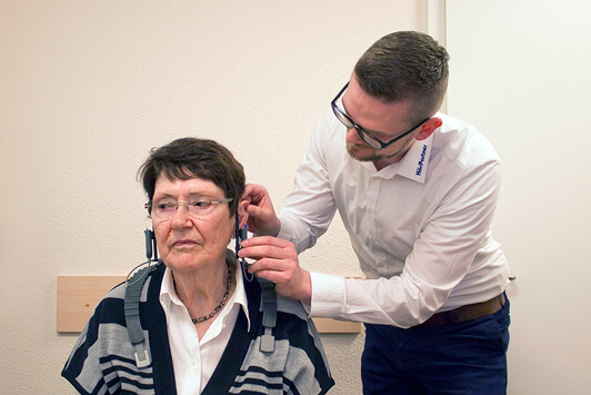 Ein Hörakustiker passt einer älteren Frau ein Hörgerät zur Hörtestung an.