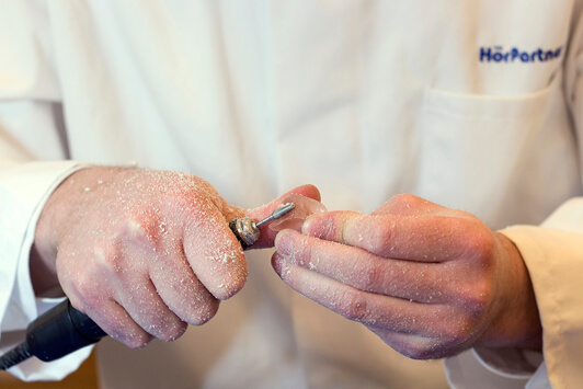 Ein Akustiker schleift ein Hörgerät, Handarbeit bei der Hörgeräteanpassung.